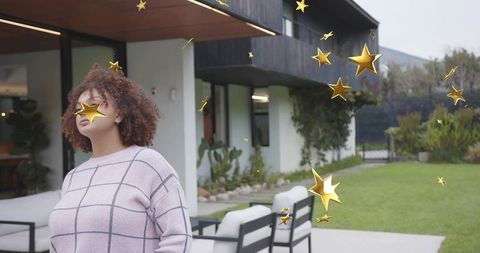 Woman standing on modern patio wearing pink grid sweater with floating gold stars