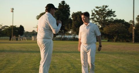 Sunlit Cricket Teammates Chatting on Grass Field During Evening Practice in White Uniforms