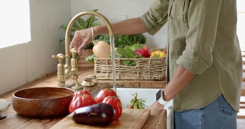 Woman rinsing fresh produce with rustic kitchen faucet