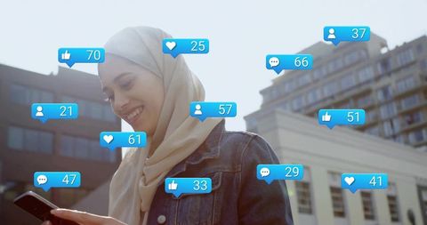 Smiling muslim woman wearing hijab checking smartphone with social notifications outdoors