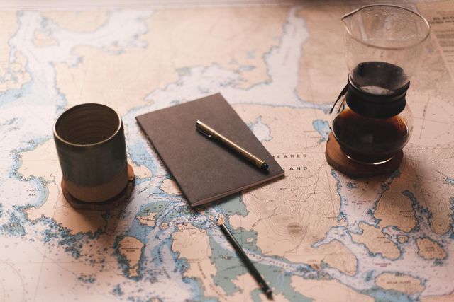 Notebook and pen placed on detailed map with coffee accessories, perfect for illustrating travel planning concepts. Suitable for blogs, travel platforms, or adventure-themed content.
