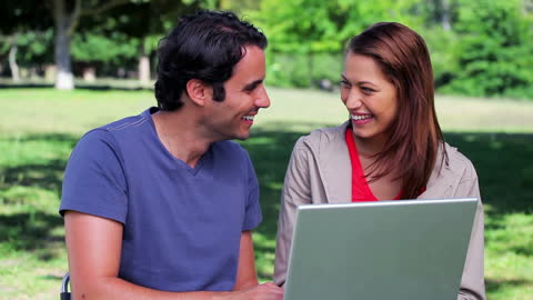 Smiling Couple Using Laptop in Lush Park Setting