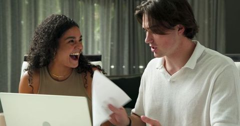 Excited Couple Reviewing Documents Using Laptop in Living Room