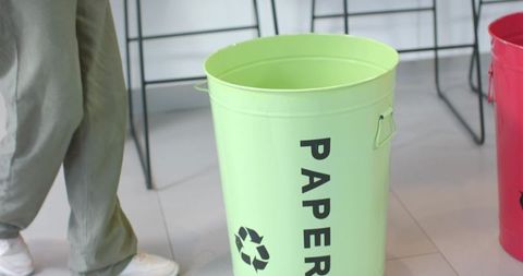 Man standing by green paper recycling bin in modern office lobby breakroom