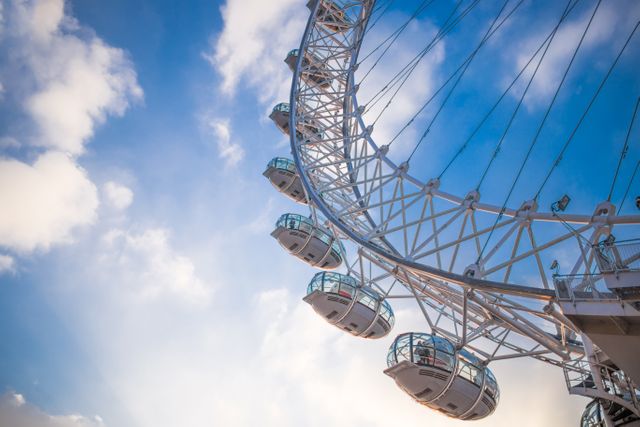 Close-up view of a modern Ferris wheel with a blue sky and some clouds in the background. Perfect for use in travel articles, brochures about tourism attractions, or advertisements for amusement parks and outdoor activities.