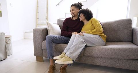 Young couple relaxing on modern sofa, cuddling and smiling in bright minimal living room