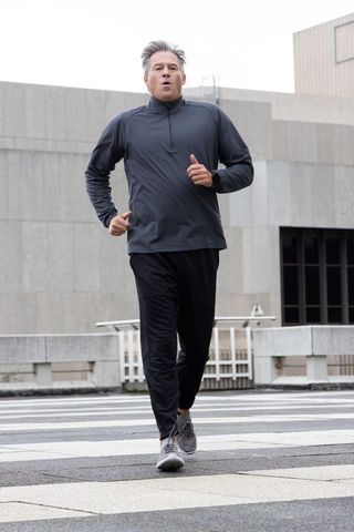 Middle-aged man running in urban plaza wearing smartwatch and dark athletic wear
