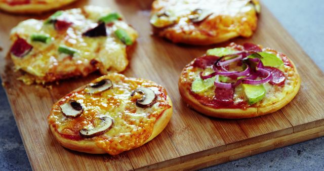 Mini pizzas with various toppings like mushrooms, pepperoni, and fresh vegetables on wooden board. Ideal for food blogs, recipe websites, party menus, advertisement for pizza products, or culinary magazines.