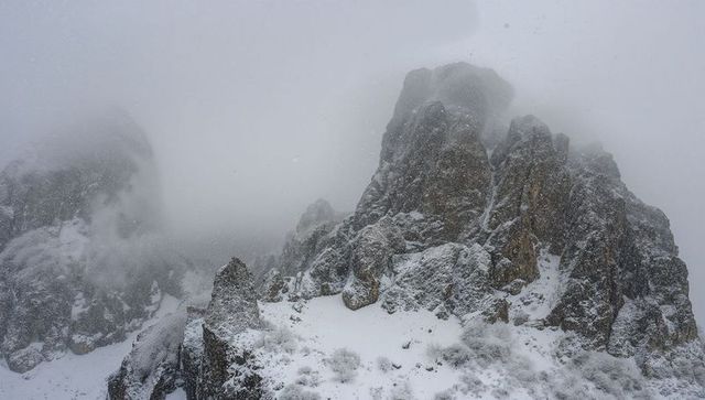 Jagged snow-covered mountain peaks looming through mist with drifting snowflakes