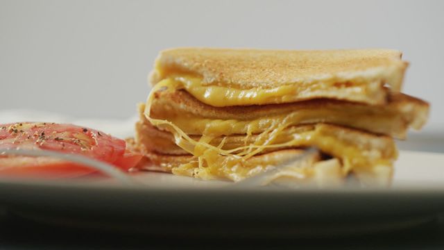 Melted cheese oozing from toasted bread, paired with fresh, spiced tomato slices, suiting a breakfast or snack theme. Perfect for use in a home cooking, brunch, or comfort food context showcasing casual meal presentations.