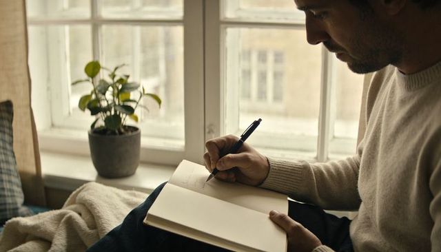 Man writing in notebook by window cozy home journaling creative planning