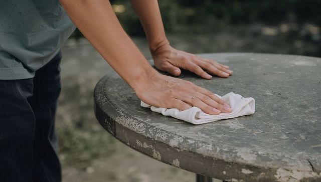 Cleaning weathered patio table with white cloth close-up hands wearing ring outdoors