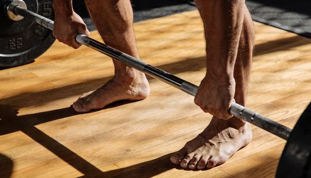 Barefoot athlete preparing deadlift on wooden platform gripping barbell strength training