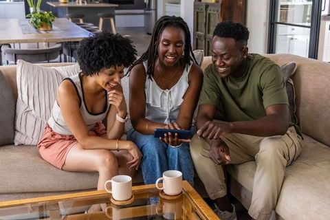 African american friends sharing smartphone laughter on cozy neutral living room sofa