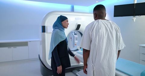 African radiographer wearing hijab guiding male patient into ct scanner in modern hospital