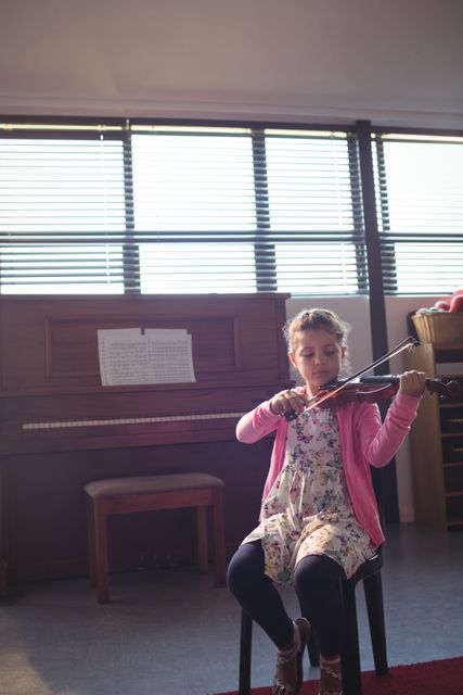 Young girl practicing violin in a music classroom, showcasing dedication and concentration. Ideal for educational materials, music school promotions, and articles on childhood learning and musical talent.