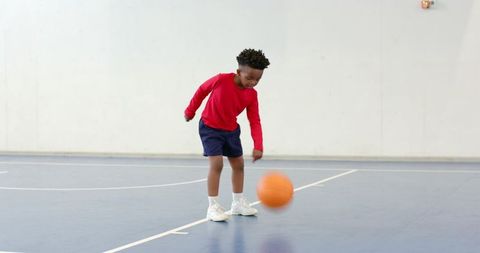 Energetic Boy Dribbling Basketball in Indoor Gym