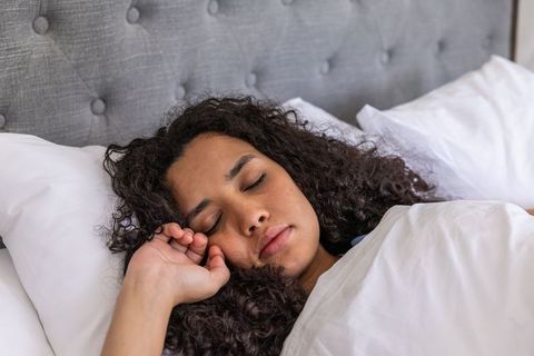 Closeup african american woman sleeping under white duvet with tufted gray headboard