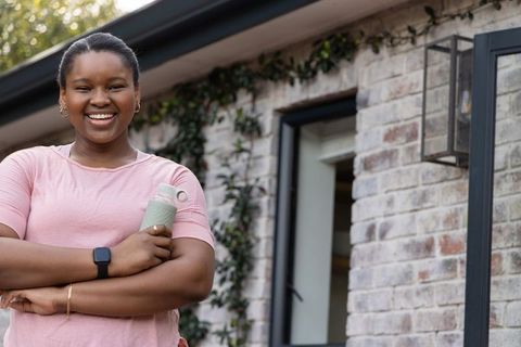 African american woman smiling on porch holding water bottle, casual lifestyle portrait