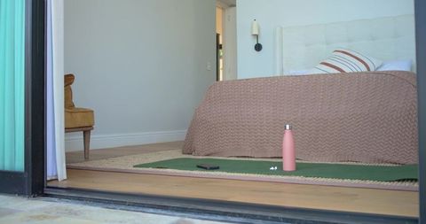 Cozy minimal bedroom with yoga mat, pink water bottle, headboard and indoor-outdoor view