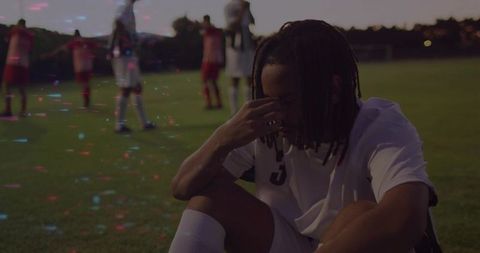 Dejected soccer player sitting on field in white jersey at sunset