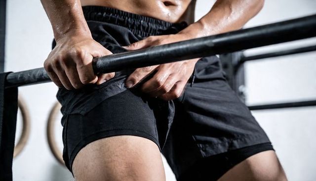 Sweaty athlete gripping pull-up bar pulling up core strength compression shorts gym intensity