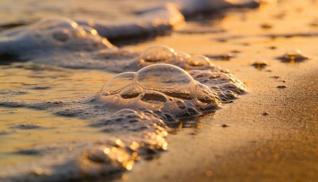 Golden sunset foam bubbles washing over sand closeup macro reflection texture warm light