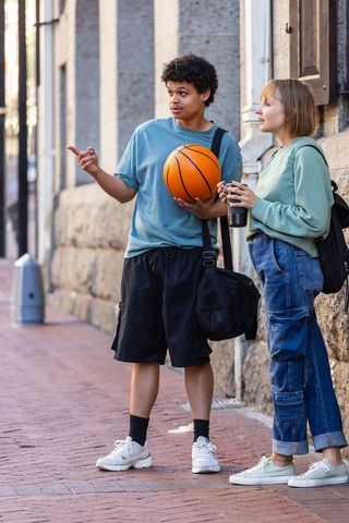 Diverse young friends chatting with basketball on urban brick sidewalk, casual campus style