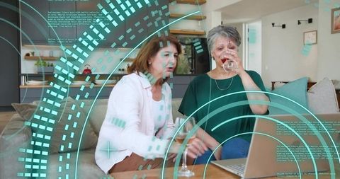 Senior mother and daughter sipping wine during virtual call on laptop with ar overlay