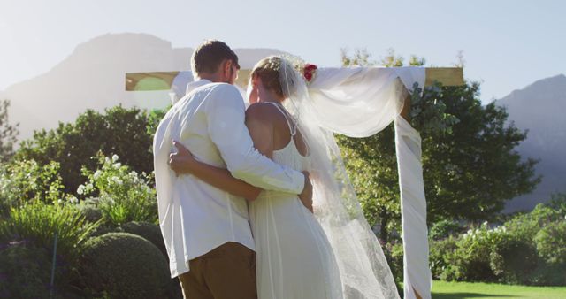 Couple embracing joyfully during a serene outdoor wedding ceremony with scenic mountainous backdrop and lush greenery. Ideal for wedding invitations, love and romance themed content, or articles on wedding planning and decorations.