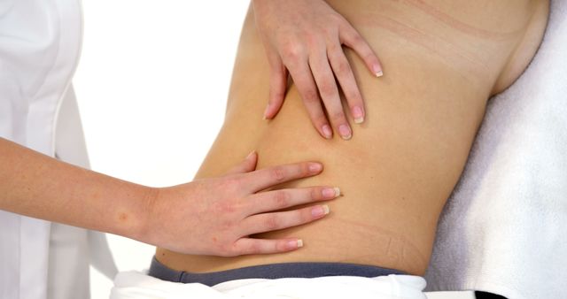 Therapist gently massaging client's back, focusing on muscle relaxation and relief. Useful for wellness blogs, physiotherapy websites, spa advertisements, and health articles promoting massage benefits.