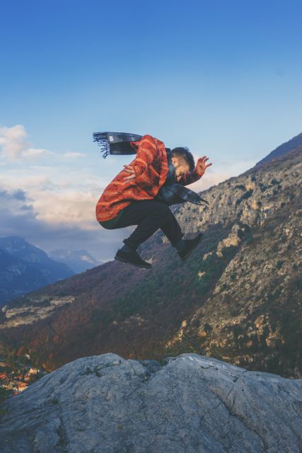 Man jumping on rocky mountainside dressed in vibrant clothing. Perfect for outdoor adventure promotions, travel blogs, and active lifestyle campaigns.