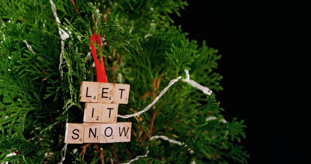 Scrabble tiles spell out Let It Snow on a festive green Christmas tree, with copy space. This holiday-themed image captures the spirit of the season with a playful message.