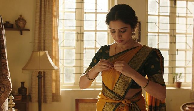 Sunlit indian woman fastening necklace in yellow saree in vintage home interior, morning