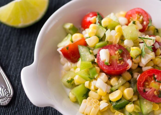 Colorful vegetable salad featuring fresh corn, cherry tomatoes, and pieces of cucumber, garnished with a slice of lime. Ideal for use in health and nutrition articles, summer recipe blogs, vegetarian meal inspirations, and healthy lifestyle promotions.