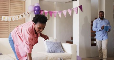 African American couple decorating living room with purple birthday balloons and banner