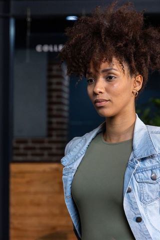 Young african american woman standing confidently in cafe wearing denim jacket and olive top