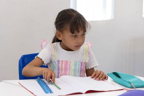 Young asian girl studying at desk with ruler and notebook concentrating on schoolwork