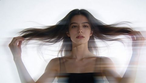 Lifting woman fanning long dark hair, creating motion blur minimalist beauty portrait
