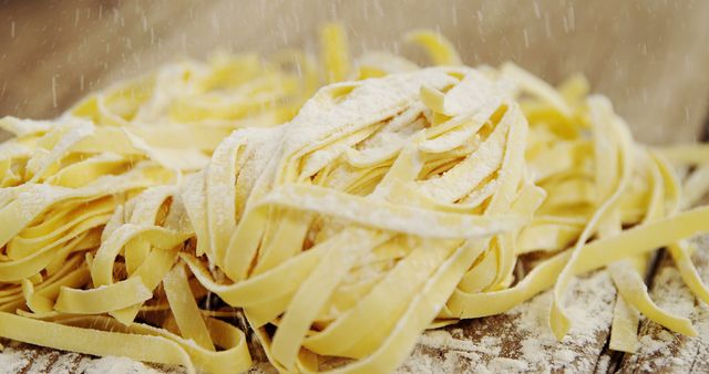 Close-up of fresh homemade tagliatelle pasta covered with a light dusting of flour on a rustic wooden surface. Ideal for use in culinary blogs, cookbooks, food advertisements, or Italian cuisine promotions.