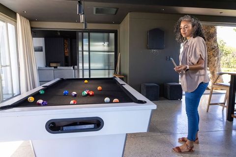 Middle-aged african woman playing pool at home holding smartphone casual lifestyle scene