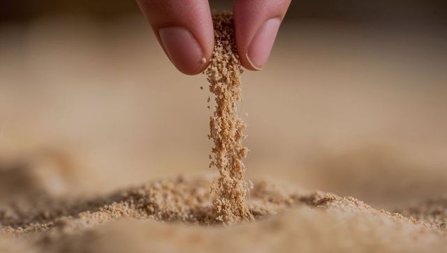 Fingers sprinkling fine sand over soft mound close-up macro texture warm beige