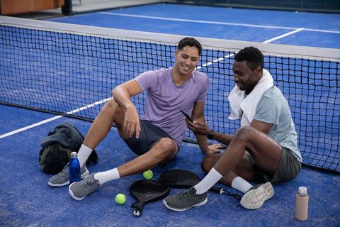 Courtside camaraderie resting and checking phone on blue padel court after match