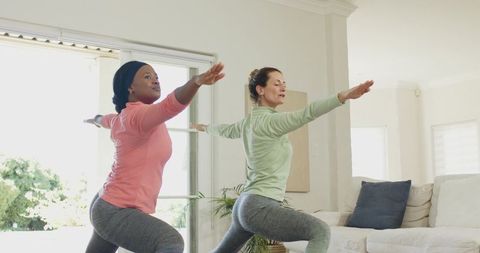 Diverse female friends practicing warrior pose in bright living room