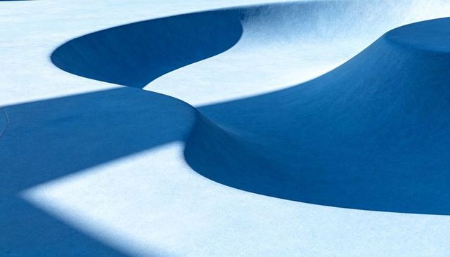 Curved blue skate bowl casting bold geometric shadows and smooth concrete texture