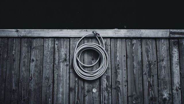 Coiled nautical rope hanging on weathered wooden dock wall with moody dark water backdrop