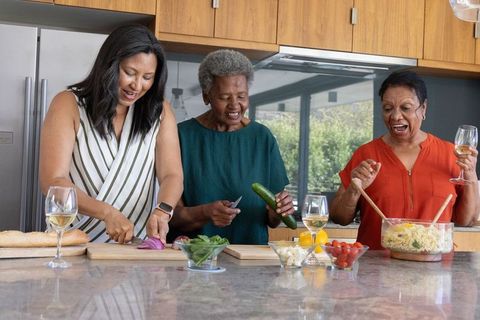 African american multigenerational women chopping, stirring and laughing in sunlit kitchen