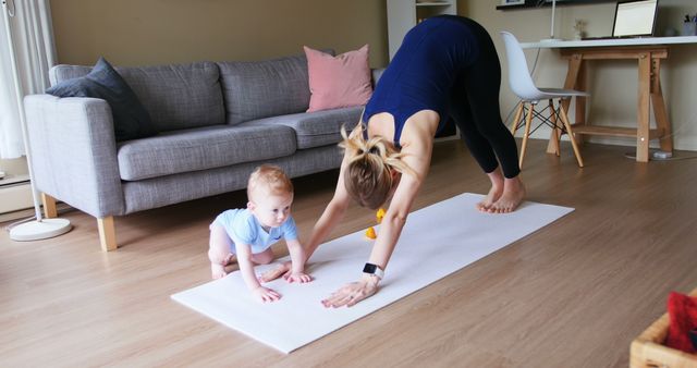 A young Caucasian woman is practicing yoga at home while her baby is sitting on the mat, with copy space. Their shared activity adds a sense of family wellness and mother-child bonding to the scene.