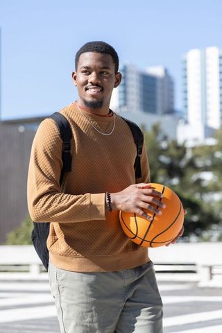 African american man standing holding basketball on urban plaza with backpack and sweatshirt