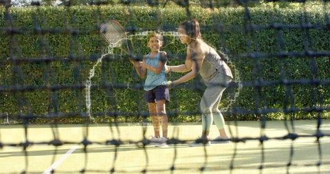 Tennis coach teaching young girl racket grip on sunny outdoor court